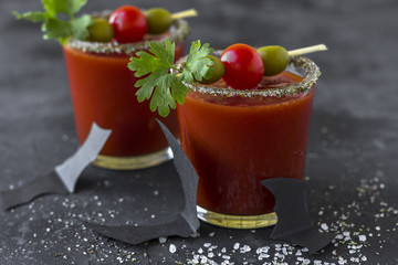 Halloween Bloody Mary cocktails served with pickled veggies (tomatos, olive and celery) and paper bats on a dark background.