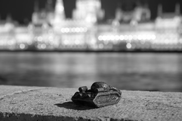 Small sculpture of tank on Danube river bank in Budapest to memorize Soviet invasion in October 1956, opposite of parliament bulding, at night, monochrome black and white