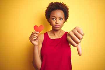 African american woman holding romantic paper hearts over yellow isolated background with angry...