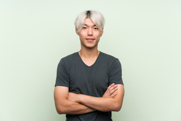 Young asian man over isolated green background keeping the arms crossed in frontal position