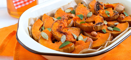 Pumpkin slices baked in the oven with honey, nuts, cinnamon, seeds, mint. Pieces of pumpkin lying on the baking paper in a bowl. Healthy food, dessert for gourmets. Traditional autumn snack