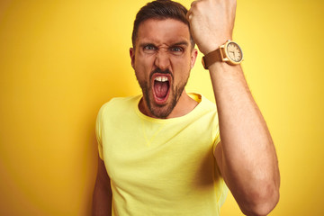Young handsome man wearing casual yellow t-shirt over yellow isolated background angry and mad...