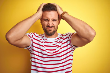 Fototapeta premium Young handsome man wearing casual red striped t-shirt over yellow isolated background suffering from headache desperate and stressed because pain and migraine. Hands on head.