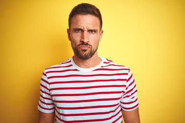 Young handsome man wearing casual red striped t-shirt over yellow isolated background skeptic and nervous, frowning upset because of problem. Negative person.