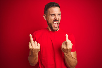 Young handsome man wearing casual t-shirt over red isolated background Showing middle finger doing...
