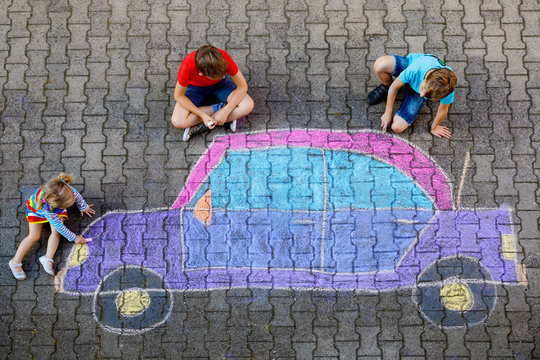 three little children, two school kids boys and toddler girl having fun with with car picture drawing with colorful chalks on asphalt. Siblings painting on ground playing together. Creative leisure