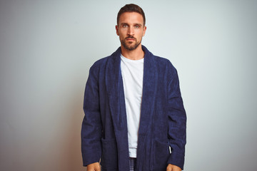 Young man wearing comfortable pajamas and robe at morning over isolated background with serious expression on face. Simple and natural looking at the camera.