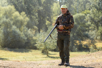 Hunting period, autumn season open. A hunter with a gun in his hands in hunting clothes in the autumn forest in search of a trophy. A man stands with weapons and hunting dogs tracking down the game.	