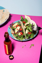 Healthy mixed salad on unwrapped tortilla, pink tabletop and blue background. Abstract healthcare conception.