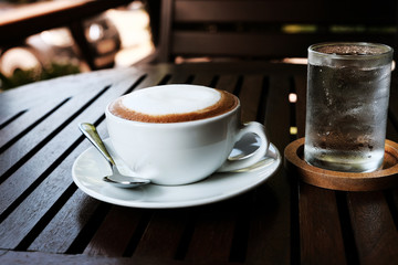 Hot cappuccino with cold water on a wooden table