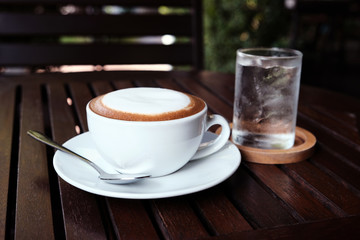 Hot cappuccino with cold water on a wooden table