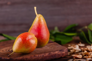 Two fresh red pears with homemade dried fruit chips on wooden background with green leaves. Concept of healthy and vegan food. Copy space.