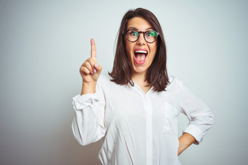 Young beautiful business woman wearing glasses over isolated background pointing finger up with successful idea. Exited and happy. Number one.