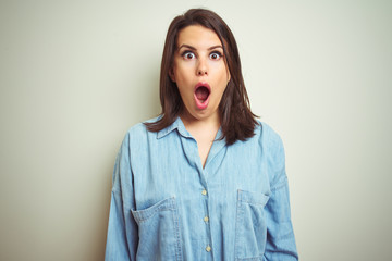 Young beautiful brunette woman wearing casual blue denim shirt over isolated background afraid and shocked with surprise expression, fear and excited face.