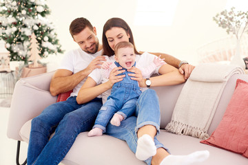 Lovely family with their baby girl relaxing on sofa at home during Christmas