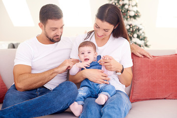 Lovely family with their baby girl relaxing on sofa at home during Christmas