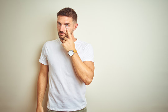 Young handsome man wearing casual white t-shirt over isolated background Pointing to the eye watching you gesture, suspicious expression