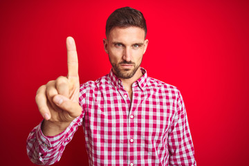Young handsome man over red isolated background Pointing with finger up and angry expression, showing no gesture