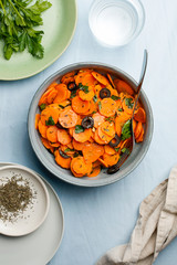 Traditional Moroccan cooked carrot salad North African vegan dish with chopped parsley and olives on gray plate top view flat lay.Healthy organic food for holiday dinner.Vertical orientation