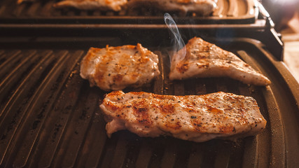 Roasting Fuming Chicken or Turkey Meat Fillets Seasoned with Spices on Electric Grill Plate.