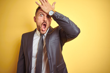 Young handsome business man over yellow isolated background surprised with hand on head for...