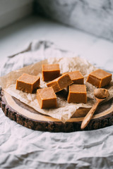 Fresh caramel fudge candies on a wooden plate with copy space in marble background