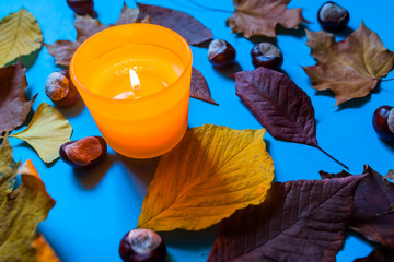 Fototapeta na wymiar Burning yellow candle surrounded by autumn leaves and chestnuts lying on vivid blue background. Stylish autumn top view. Hello autumn. Fall background. Autumn background.