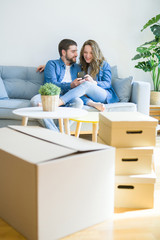 Fototapeta na wymiar Young couple in love hugging sitting on the sofa using smartphone very happy moving to a new home