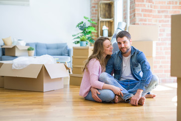 Young beautiful couple in love sitting on the floor together with cardboard boxes around for moving to a new house
