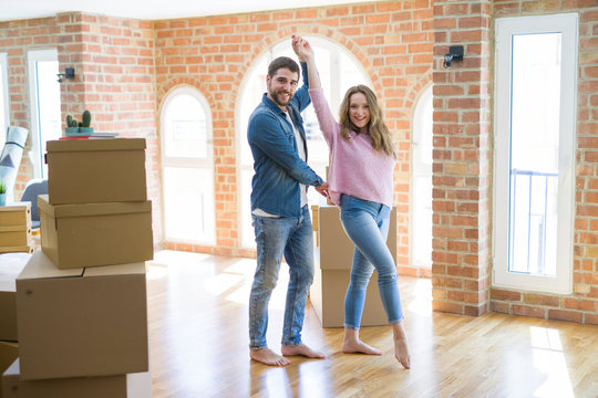 Young couple dancing celebrating moving to new apartment around cardboard boxes