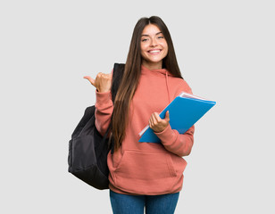 Young student woman holding notebooks pointing to the side to present a product over isolated grey background