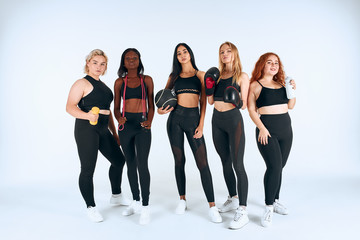 Fototapeta premium Young different girls in sportive wearing posing, look at camera, holding boxing gloves, dumbbells, sportive things