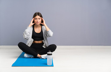 Fototapeta premium Young sport woman sitting on the floor with mat unhappy and frustrated with something. Negative facial expression