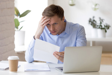 Stressed middle aged businessman reading paper document with bad results.