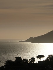Silhouette of the castle of Lerici at sunset. Sky with clouds and sea of gold color.