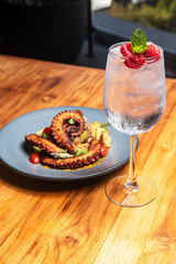 Delicious glass of gin with raspberry, accompanied by a plate of octopus with vegetables