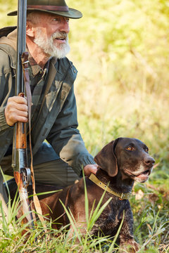 Hunting season. Senior hunter man with gun sit on ground with labrador. Hunting concept