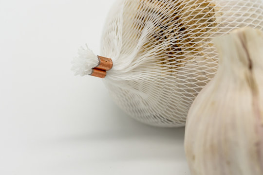 Close-up image of dried Garlic bulbs shown with the white plastic netting in which they are packaged in. Shown on a kitchen table, as part of a food additive. The dried roots are also visible.