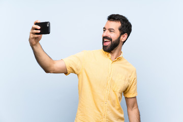 Young man with beard over isolated blue background making a selfie