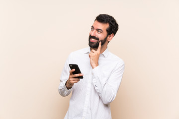 Young man with beard holding a mobile thinking an idea while looking up