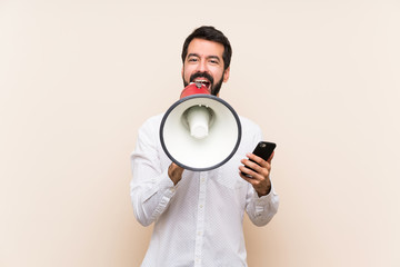 Young man with beard holding a mobile shouting through a megaphone