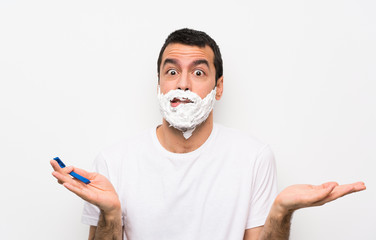 Man shaving his beard over isolated white background having doubts while raising hands