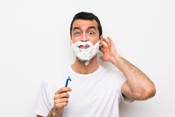 Man shaving his beard over isolated white background having doubts