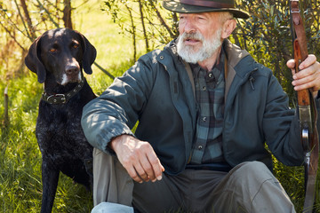 Mature bearded man after hunting in autumn forest, sit having rest