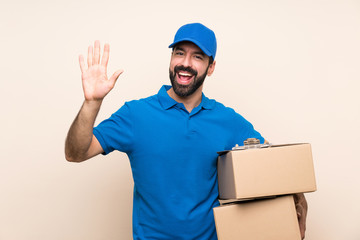 Delivery man with beard over isolated background saluting with hand with happy expression