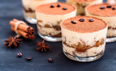 gourmet tiramisu dessert in a glass sprinkled with cocoa and decorated with coffee beans on a dark background, luxury dessert