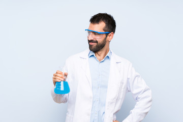 Young scientific holding laboratory flask over isolated background posing with arms at hip and smiling