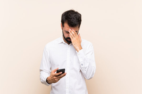 Young man with beard holding a mobile with tired and sick expression