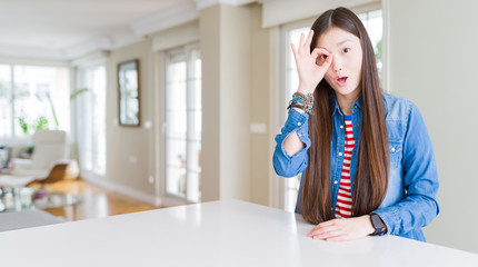 Fototapeta na wymiar Young beautiful asian woman with long hair wearing denim jacket doing ok gesture shocked with surprised face, eye looking through fingers. Unbelieving expression.