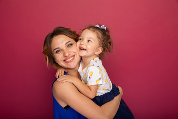 Mother holding little daughter on the hands and smiling standing in a bright studio